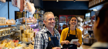 Two sales associates smiling at a customer in a cheese shop