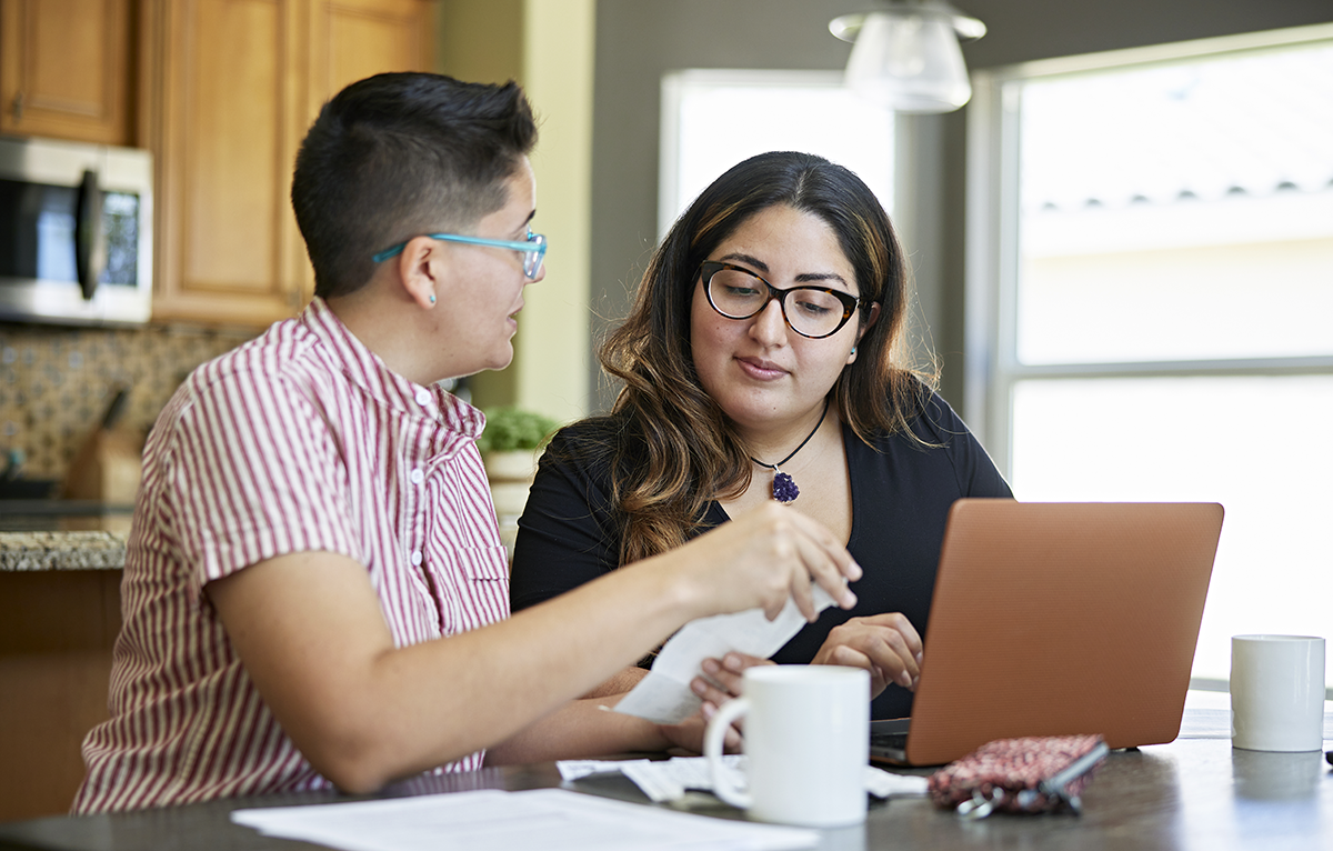 Two people at home with laptop, reviewing bills and receipts